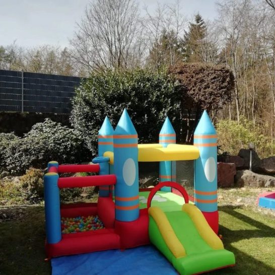 Bunte aufblasbare Hüpfburg mit Rutsche in einem Garten.